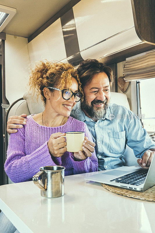 Modern couple use together laptop inside camper van. Computer leisure people surfing the web. Traveler planning next destination smiling and enjoying freedom living off grid. Digital nomad concept